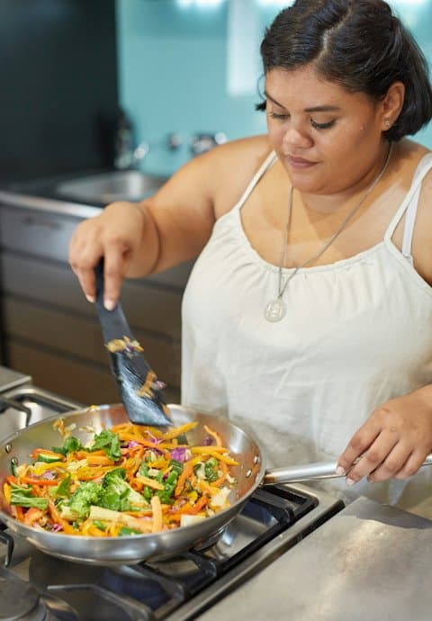 A food creator stirring a colourful vegetable stir-fry at her stove while filming a recipe Reel