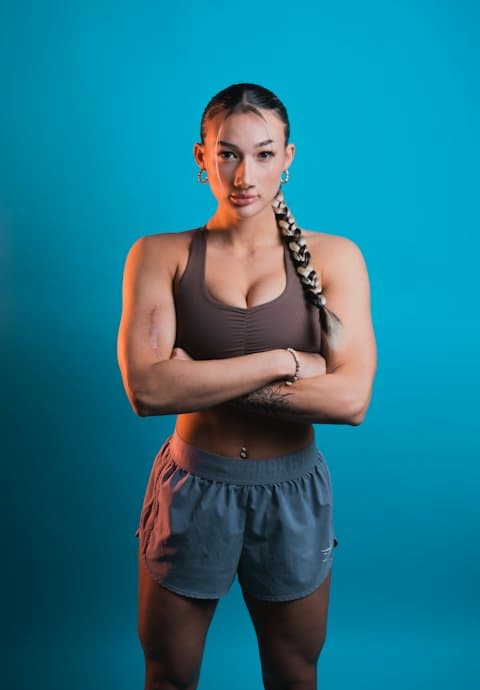 A fitness creator in gym wear standing with arms crossed against a bright teal studio backdrop
