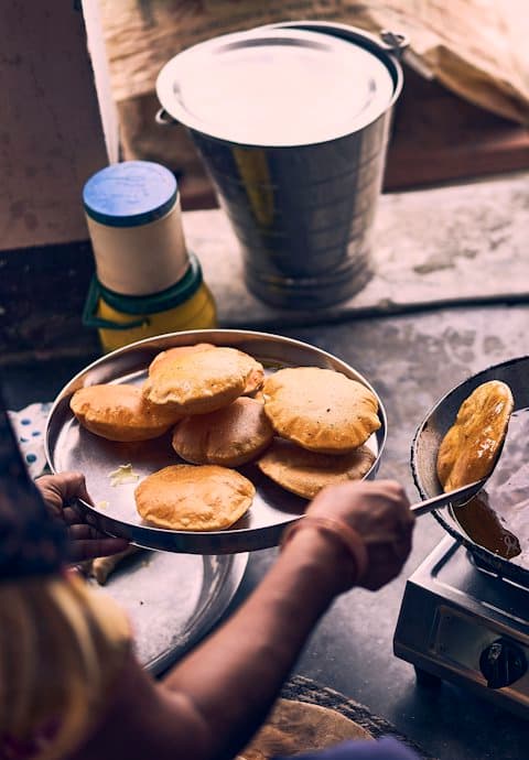 A street food cook frying golden puris in a pan and stacking them on a steel plate